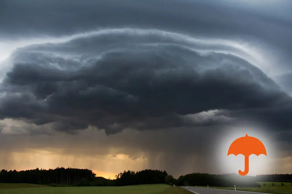 Dunkle Gewitterwolken über einer Landschaft mit orangefarbenem Regenschirm-Symbol
