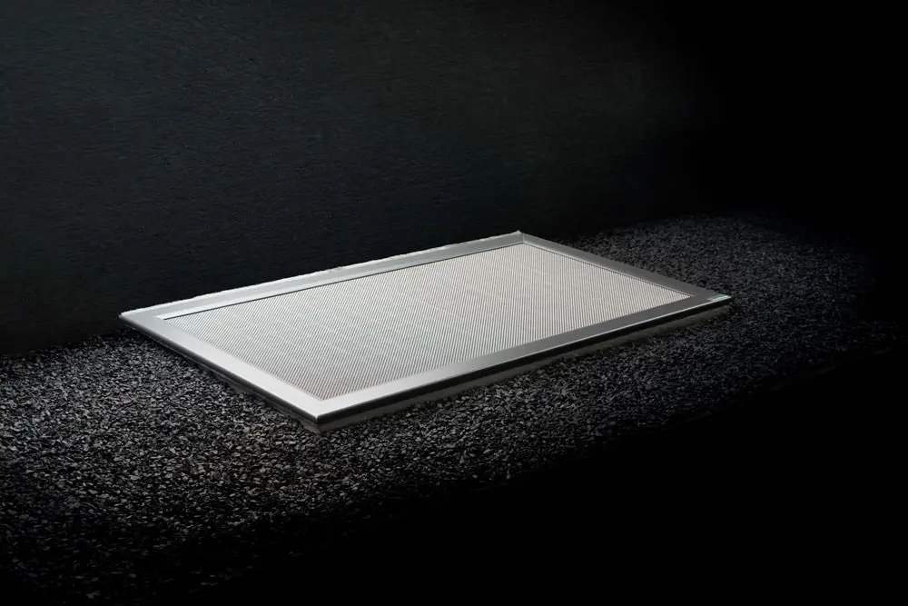 ShadowLine Lichtschachtabdeckung auf dunklem Splitt, Rahmen und Gittereinsatz sichtbar
